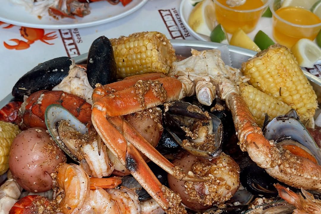 A seafood boil with snow crab legs, mussels, shrimp, corn and potatoes, with drinks and lemon wedges behind