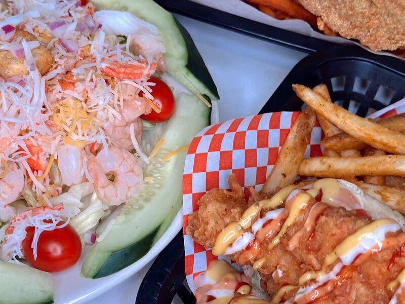 A fried Po Boy with fries, a shrimp salad and a fried fish basket with sweet potato fries