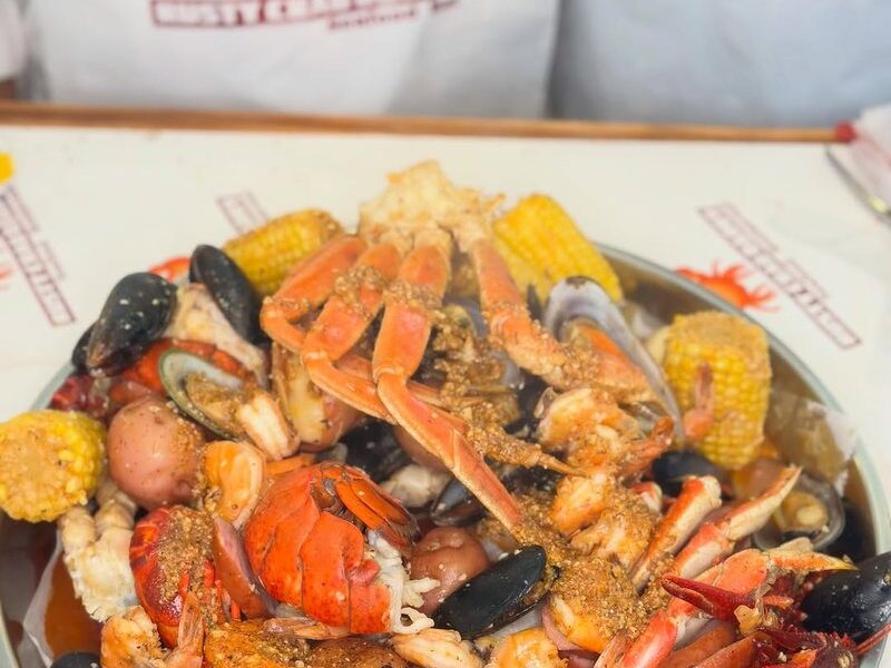 A shared seafood boil tray with crab, lobster, corn and egg