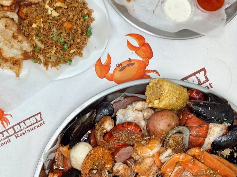 Overhead view of a seafood boil tray, a plate of fried rice and a fried basket on crab-print paper